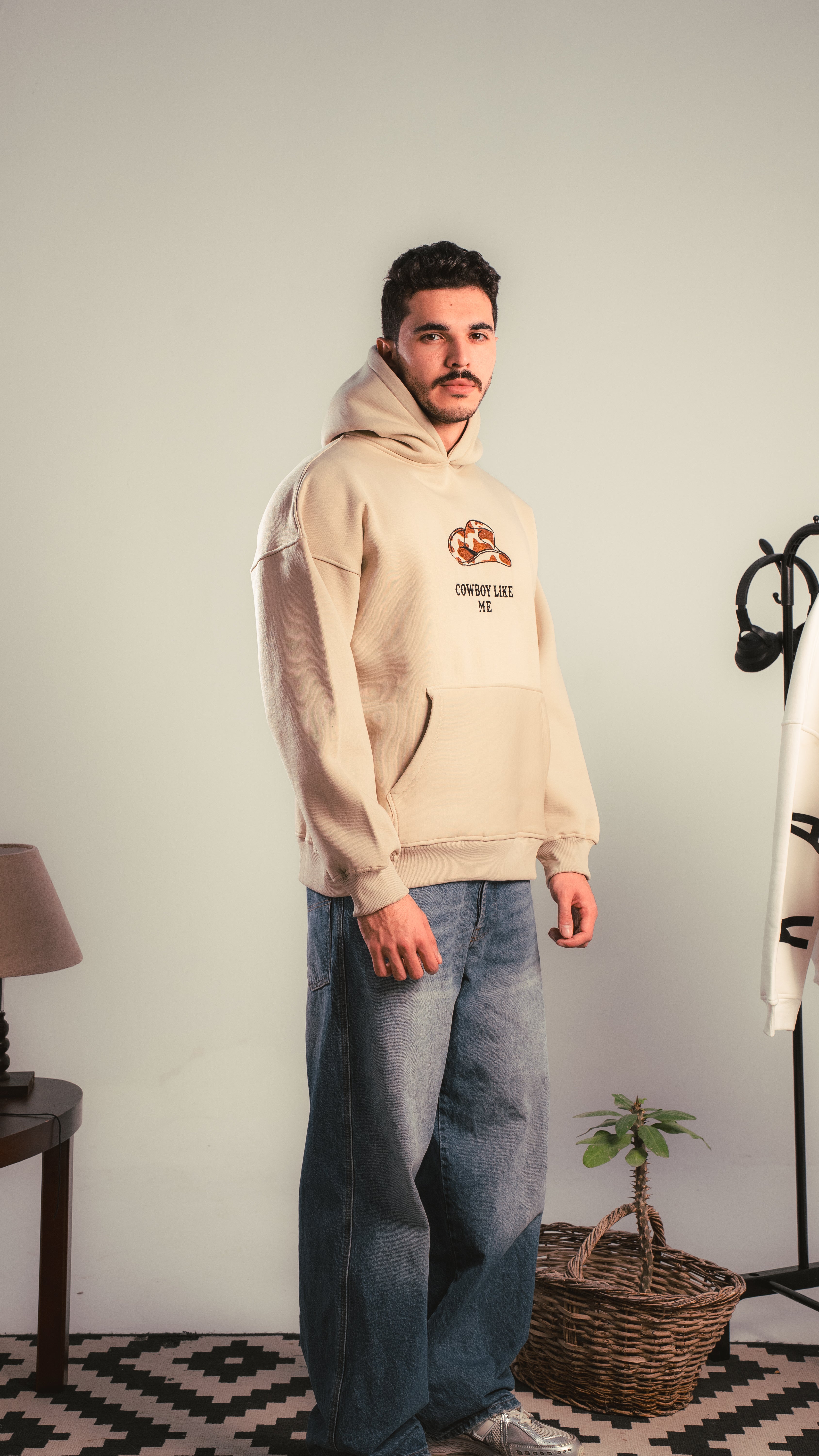 Side view of a person wearing a beige hoodie with ‘Cowboy Like Me’ graphic