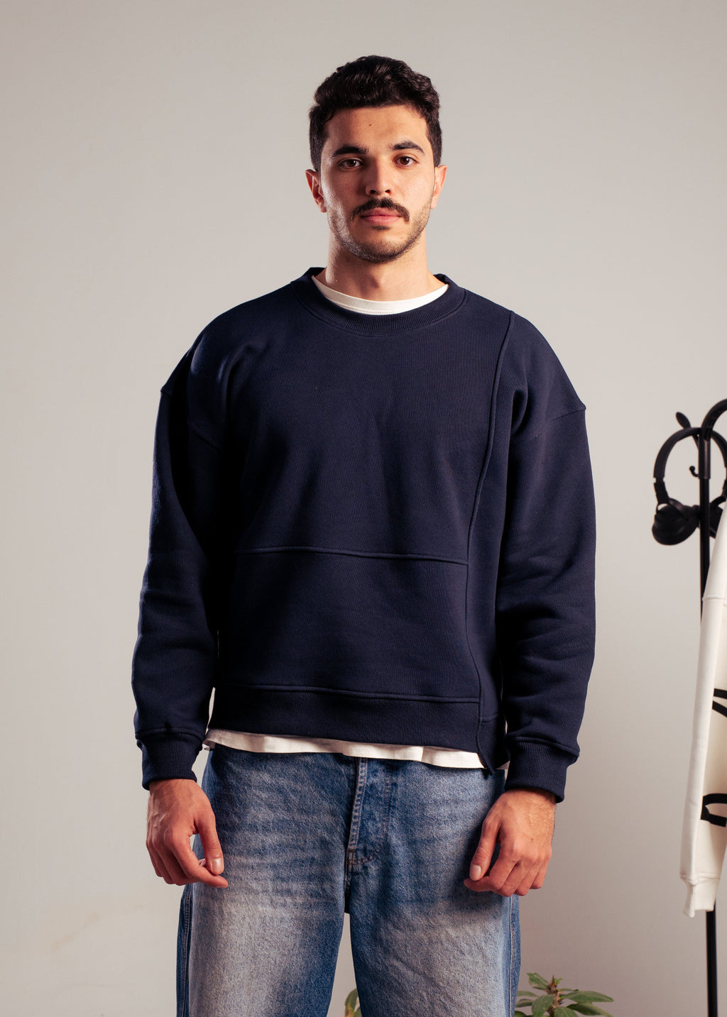 Man wearing a navy sweatshirt from Kalium, standing indoors on patterned carpet.
