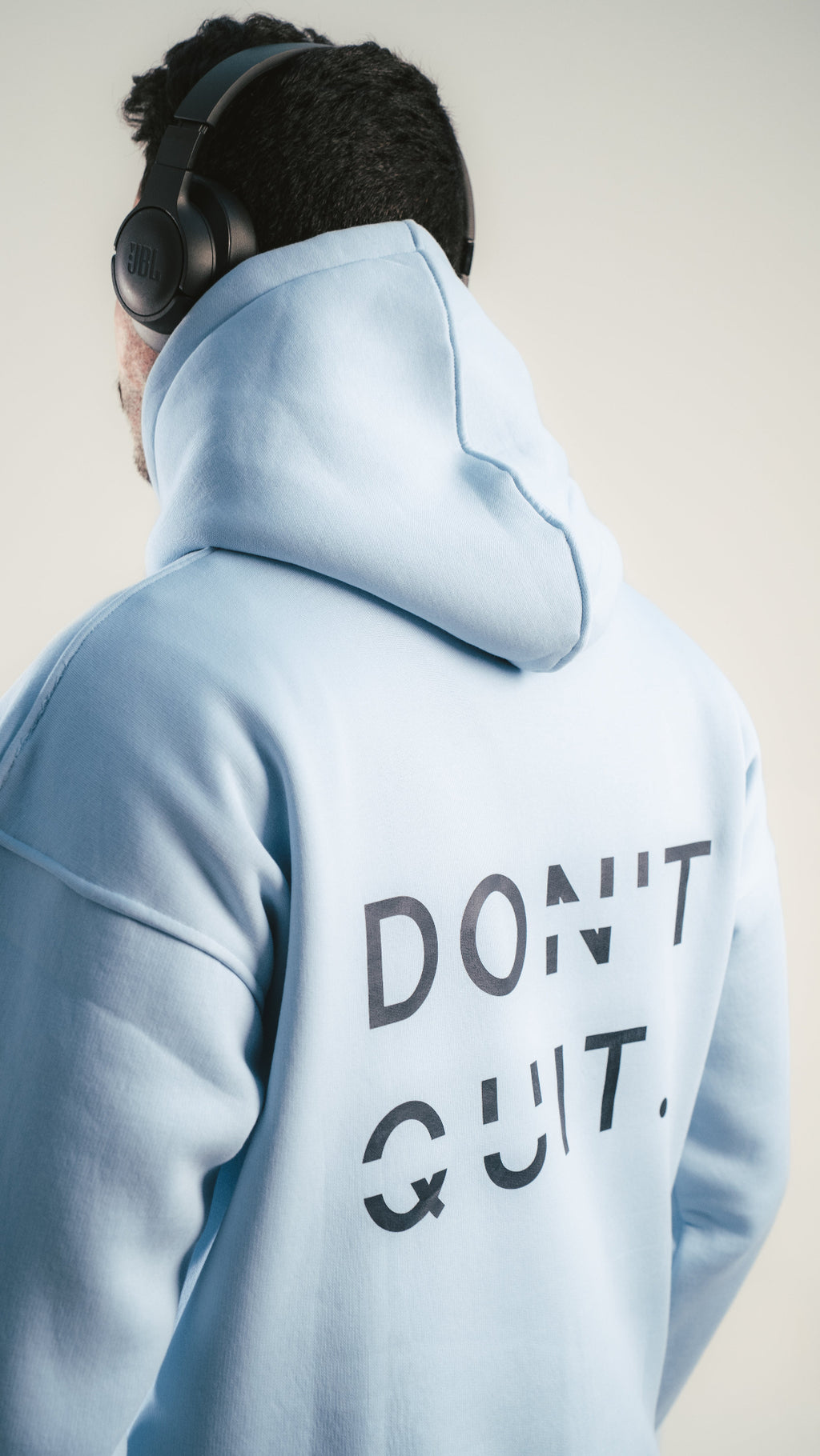 Person wearing a light blue hoodie with 'DON'T QUIT' text on the back, against a plain background.
