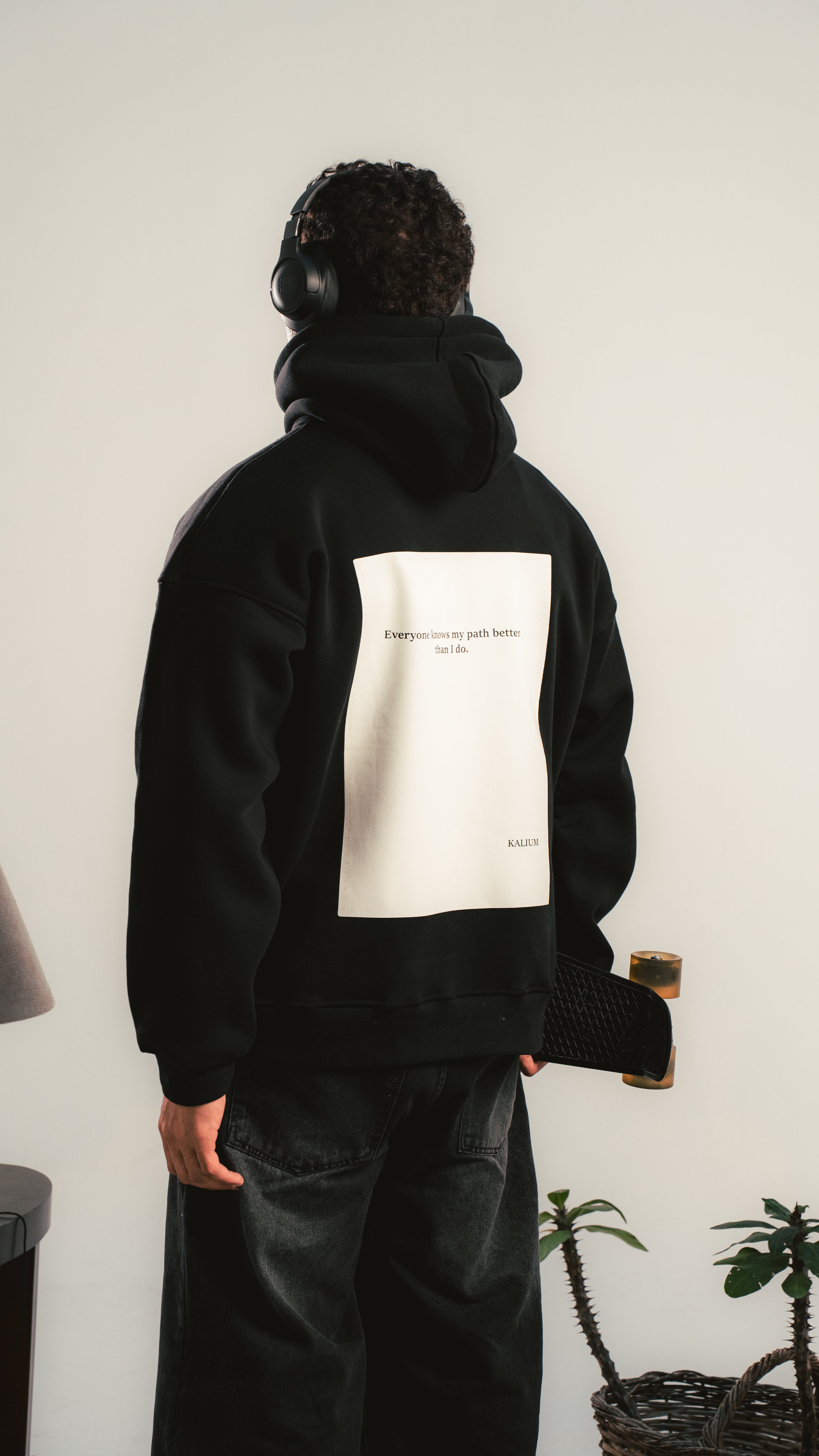 Person wearing a black hoodie with a white graphic on the back, standing against a plain wall.
