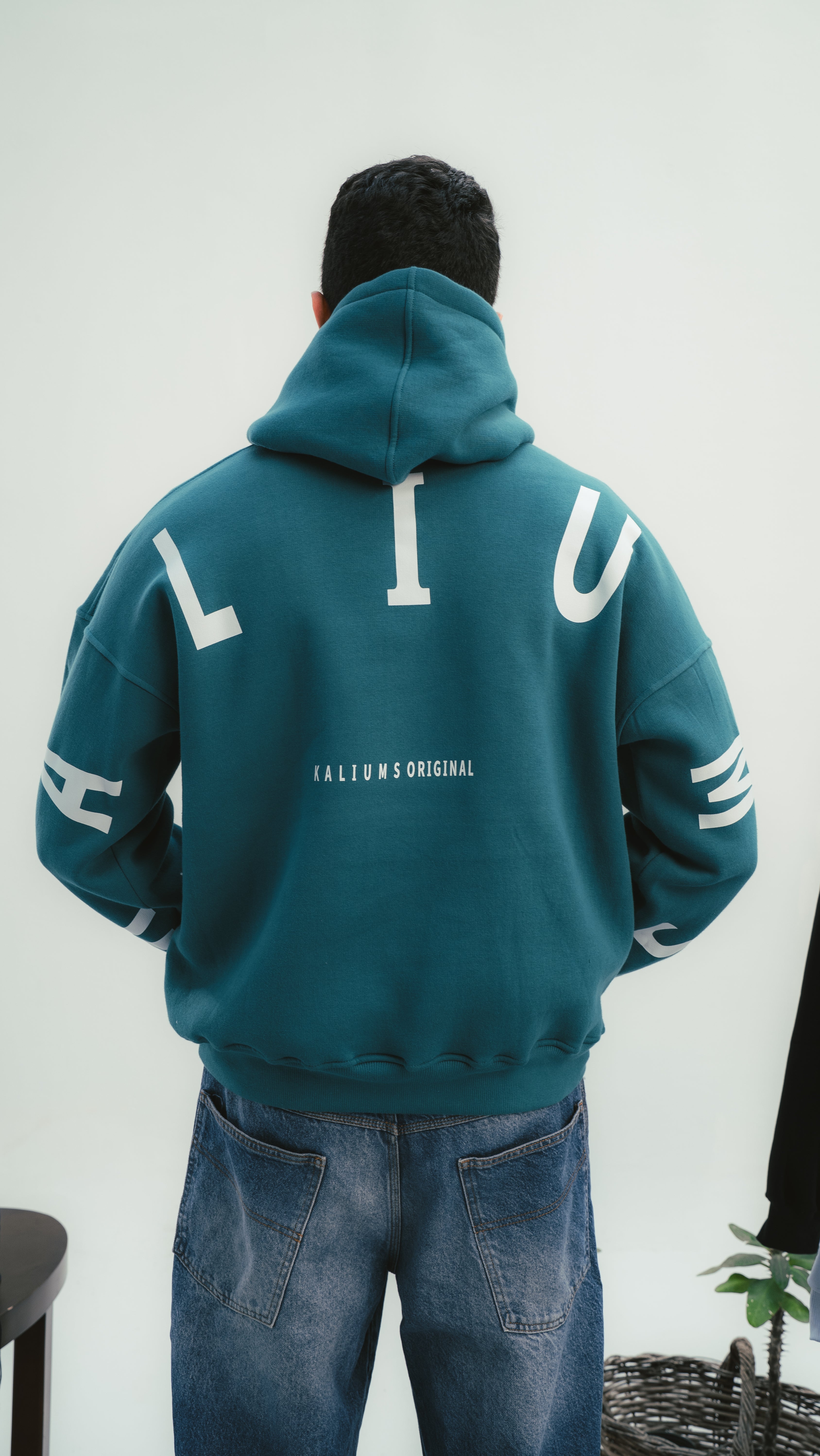 Person wearing a teal hoodie with white text on the back against a white background