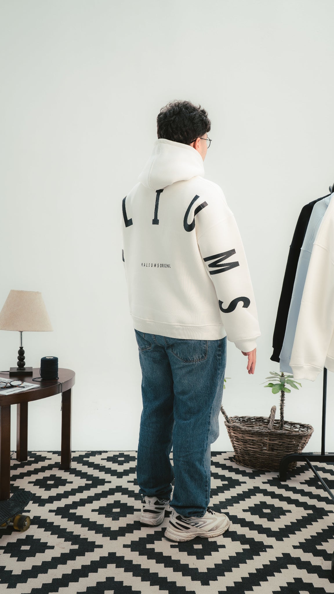 Person wearing a white hoodie with black text standing in a room with a geometric patterned rug.