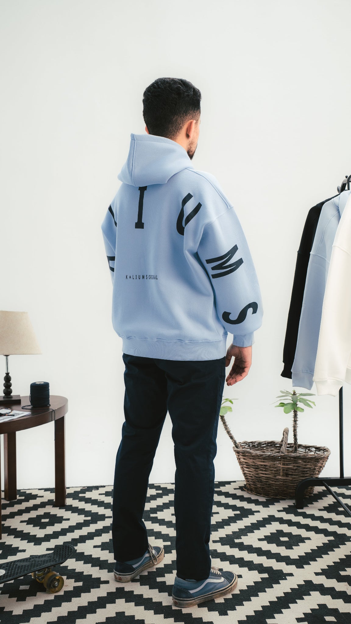 Person wearing a light blue hoodie with black text, standing in a room with a geometric patterned rug.