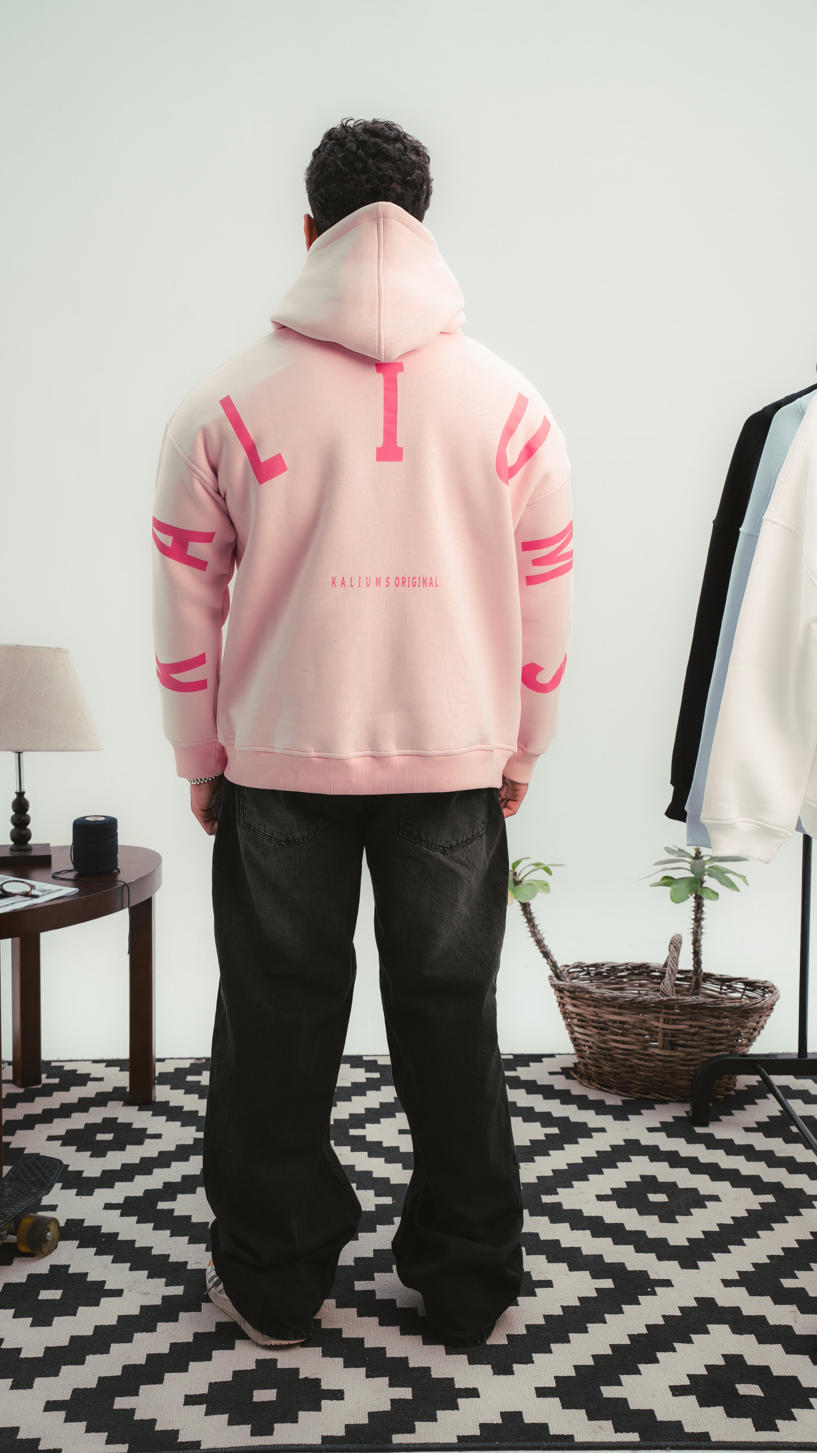 "شاب يرتدي هودي وردي من Kalium بتصميم الحروف الكبيرة على الظهر — لقطة خلفية واضحة